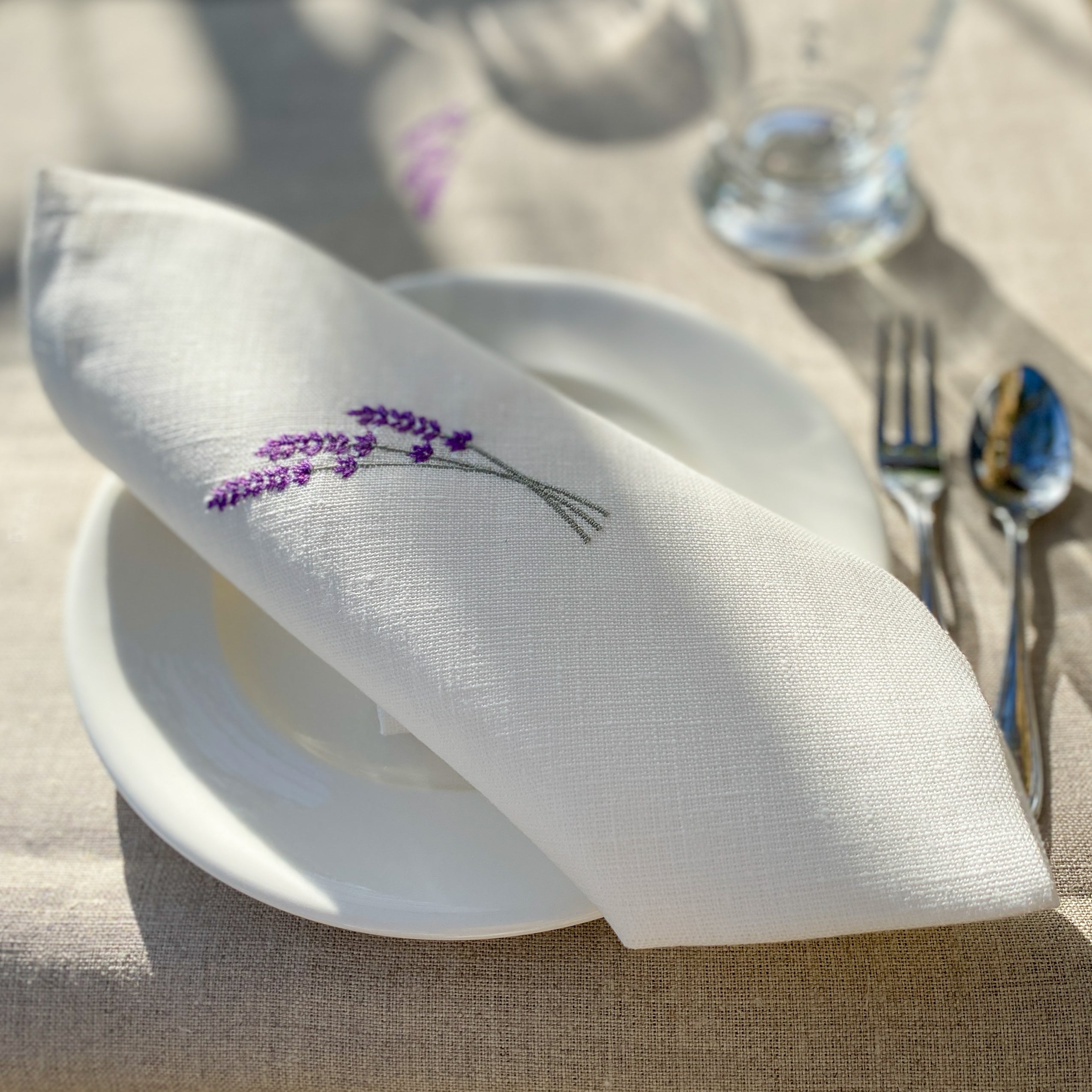 Leinenserviette mit zarter Lavendelstickerei, handgefertigt in unseren Werkstätten in Südfrankreich. Präsentiert auf einem stilvoll gedeckten Tisch – ideal für eine natürliche, elegante Tischdekoration.