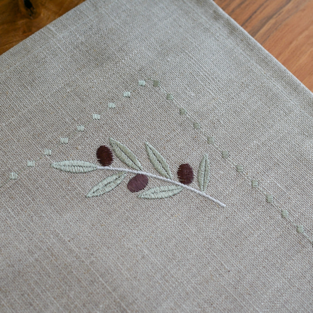 Tischset aus 100 % gewaschenem Leinen in Naturton, verziert mit einem feinen olivfarbenen Stickmuster. Das dezente Design bringt mediterrane Eleganz und handwerkliche Raffinesse auf den gedeckten Tisch.